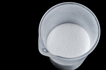 white crumbly refined sugar in containers on a black background, isolate .