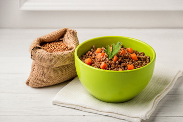 Green bowl of tasty buckwheat porridge on white wooden table.