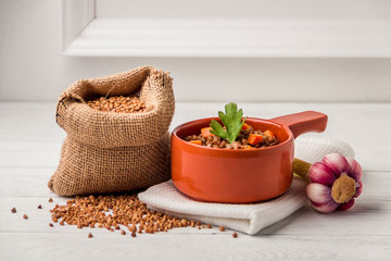 Brown bowl of tasty buckwheat porridge on white wooden table.