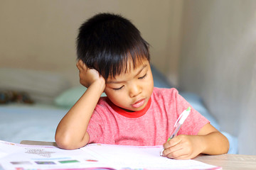 Naklejka premium Asian child boy doing homework. He writing on a book. Kid and education concept.