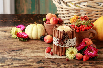 Candle decorated with cinnamon sticks among autumn fruits and flowers.