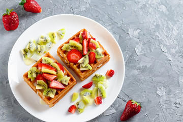 Belgian waffles with fruits strawberries and kiwi on white plate closeup