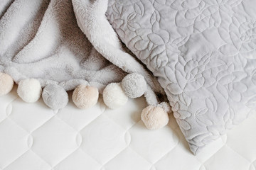Grey blanket with pompoms on the new mattress.