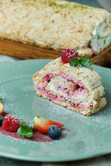 Meringue cake roll slice on a plate with berries, on a gray background