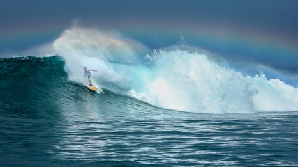 Surfer riding big green wave with rainbow in background in North Maluku islands, Indonesia	