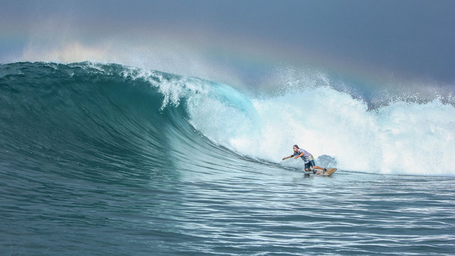 Surfer Riding Big Green Wave With Rainbow In Background In North Maluku Islands, Indonesia	