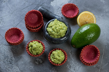 Guacamole dip sauce with vegetable tartlets, elevated view over grey concrete background