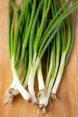 Fresh green onions on a bamboo board, side view.