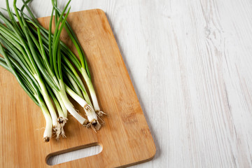Fresh green onions on a bamboo board over white wooden background, low angle view. Copy space.