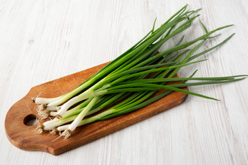 Fresh green onions on a cutting board over white wooden background, side view. Close-up.