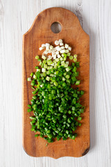 Chopped green onions on a rustic wooden board, overhead view. Top view, flat lay, from above. Close-up.