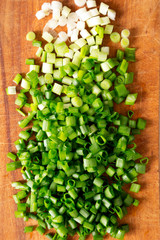 Chopped green onions on a rustic wooden board, view from above. Top view, flat lay, overhead. Close-up.