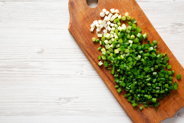 Chopped green onions on a rustic wooden board on a white wooden background, top view. Overhead, flat lay, from above. Copy space.