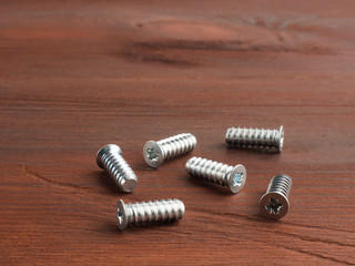 Set of silver color steel screws on a brown wooden background
