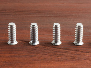 Set of four silver color steel screws on a brown wooden background