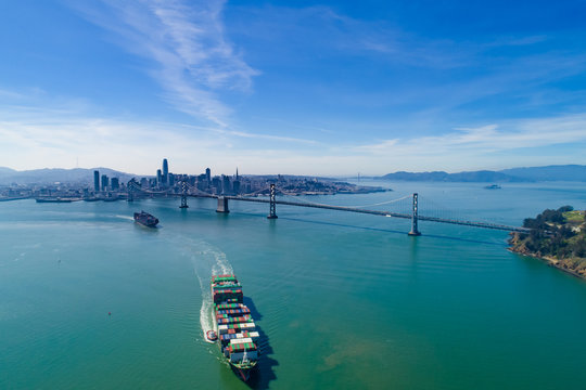 Cargo ships with containers navigating the San Francisco bay  with the Bay Bridge and the city background