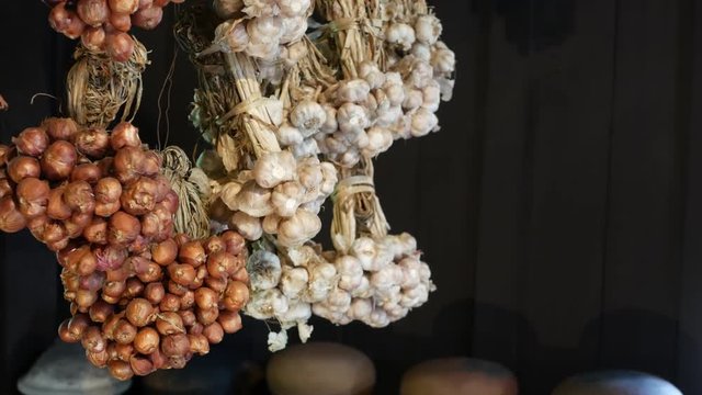 Dried onion and garlic in kitchen. Bunches of small dried onion and garlic hanging against dark wooden wall in kitchen