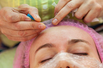 A young girl is lying on a couch during cosmetic procedures with a mask on the face above which...