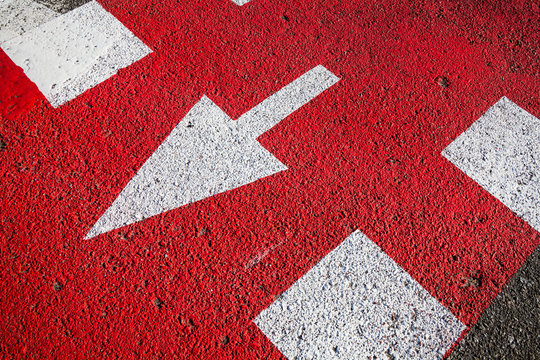 White Arrow On The Red Asphalt Surface.