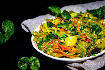 On an oblong plate is a dish of zucchini, carrots, mint, herbs, garlic. All this on a black background, mint leaves and light fabric. 