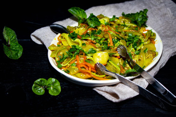 On an oblong plate is a dish of zucchini, carrots, mint, herbs, garlic. All this on a black background, mint leaves and light fabric. 