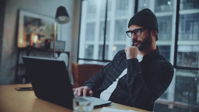 Bearded hipster working into process of startup project creating in coworking space. Man wearing eye glasses and using laptop at office