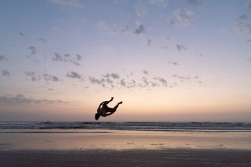 Silhouette of young boy performing stunts in front of sea