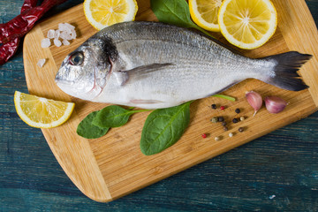 Raw fresh dorado fish on a cutting board with lemon and spices. View from above.