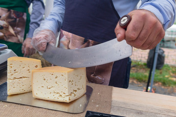 Seller cutting delicious cheese on table in store. Food