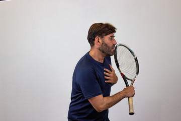 Portrait of handsome young man playing tennis holding a racket with brown hair suffering, facing forwards and looking at the side. Isolated on white background.