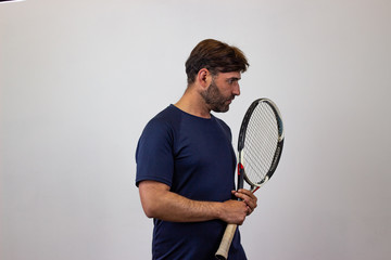 Portrait of handsome young man playing tennis holding a racket with brown hair showing bad face,...