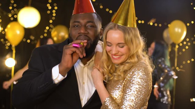 Positive male and female friends celebrating new year night club, blowing horn