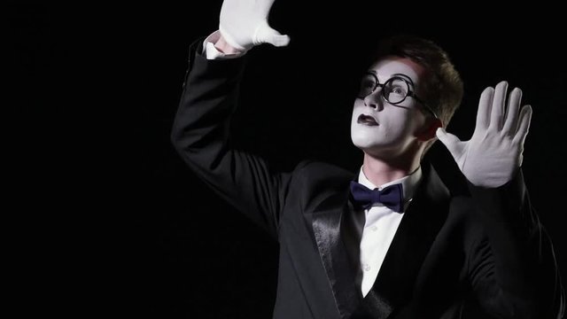 Young mime man behind an invisible glass wall on black background