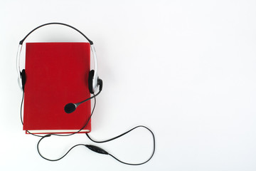 Audiobook on white background. Headphones put over red hardback book, empty cover, copy space for ad text. Distance education, e-learning concept.