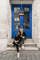 Fototapeta na wymiar Attractive woman tourists in old european city. Beautiful young girl standing near the ancient blue door. Stylish teens traveling and enjoying summer time in Lviv, Ukraine. Girls in black 