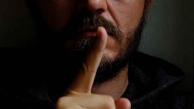 Don't speak, be quiet - close up portrait of bearded man on the door saying shhh. Finger on lips. Head and shoulders, no eyes. Danger. Violence concept.
