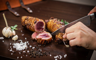 slicing organic roast beef roll on wood table with ingredients