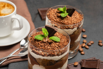 Classic tiramisu dessert in a glass and cup of coffee on dark concrete background