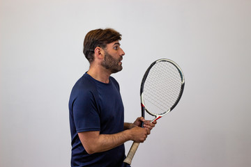 Portrait of handsome young man playing tennis holding a racket with brown hair looking jealous,...
