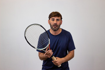 Portrait of handsome young man playing tennis holding a racket with brown hair indignant, looking at the camera. Isolated on white background.