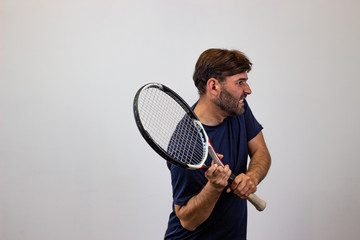Portrait of handsome young man playing tennis holding a racket with brown hair looking with rage,...