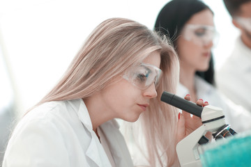 close up.serious female scientist looking into microscope in lab