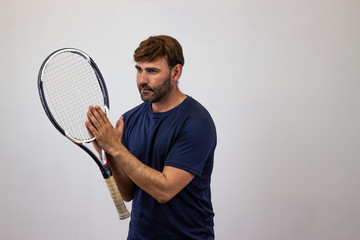 Portrait of handsome young man playing tennis holding a racket with brown hair vulnerable, facing forwards and looking at the horizon. Isolated on white background.