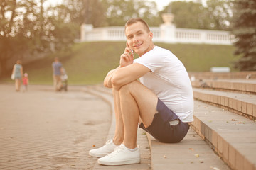 young man talking on a mobile phone, sitting on the steps in the city Park