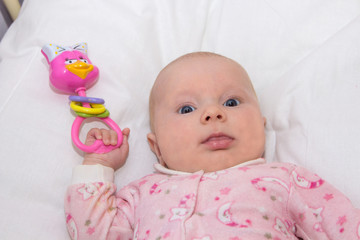 newborn with developing toy,Lying on the bed is a beautiful newborn baby girl with a rattling toy in her hands