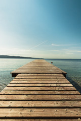 Wooden pier leading towards the shallow water in a picturesque bay with beautiful clear blue sky and calm azure water (Corfu, Greece, Europe)