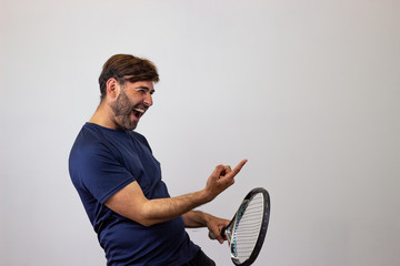 Portrait of handsome young man playing tennis holding a racket with brown hair saying no with a finger, facing forwards and looking at the side. Isolated on white background.