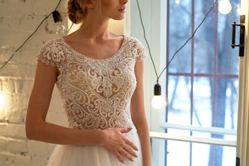 The bride in a white lace dress with embroidered bodice, indoors in loft style. High key.