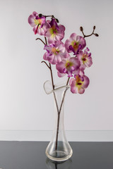 a glass vase with a bouquet of artificial orchids on a black base creating a reflection.