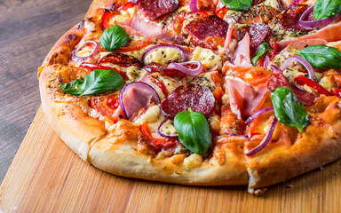 Pizza with Mozzarella cheese, ham, tomato sauce, salami, onion, pepper, Spices and Fresh basil. Italian pizza on wooden table background